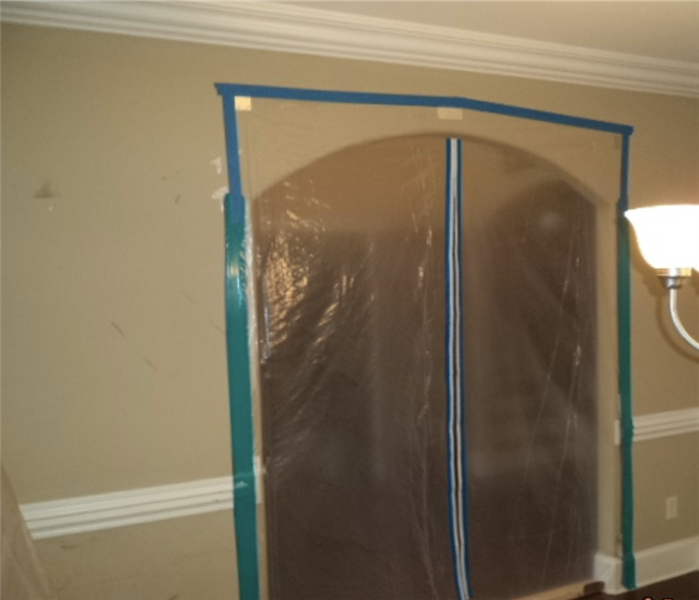 beige walls in a house, doorway frame covered in plastic sheeting and taped at all sides to contain damage in a small area
