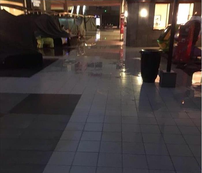 wet, flooded tile throughout the mall area where SERVPRO had a water damage call, white tile, reflection of lights, dark room