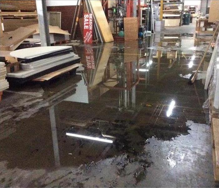 puddles of water on the cement floor of a warehouse with pallets of wood