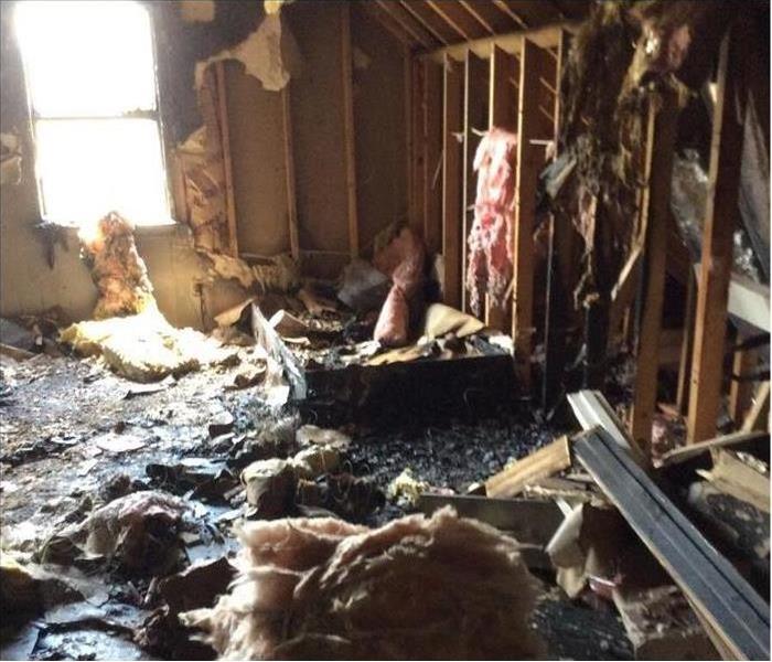 fire damage and insulation in an attic, window in the background, exposed beams and studs
