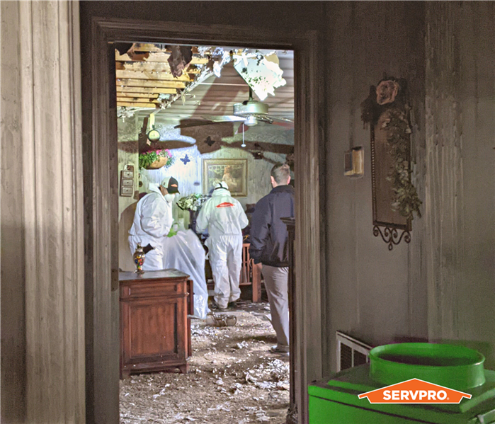 house fire, SERVPRO technicians in white PPE suits cleaning out a room that has fire damaged debris
